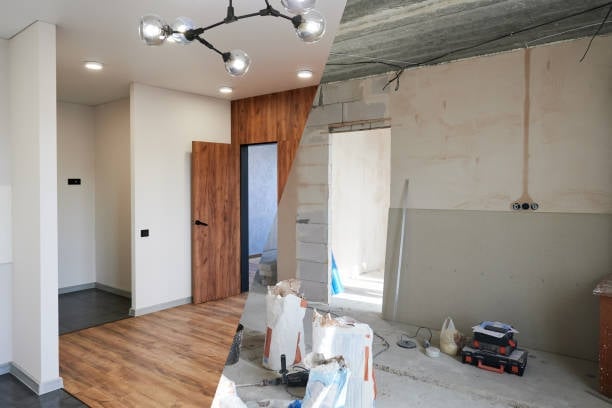 Modern apartment under renovation with white walls, wooden doors, exposed concrete ceiling, wood flooring, and construction materials scattered throughout