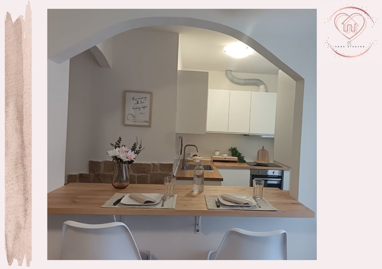 Modern kitchen pass-through with wooden counter seating, white chairs, stovetop, and flowers in a vase